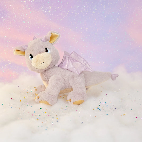 Plush dragon toy with wings on a soft, cloud-like surface with a pastel gradient background.