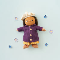 Toy figure wearing a purple coat and yellow dress on a light blue background with flowers.