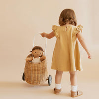 Plush baby doll with brown hair, beige romper, and brown shoes in a trolley with a kid